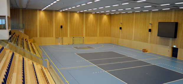 Modern idrottshall i ljusa färgtoner och ljus träpanel på väggarna.