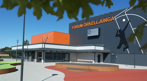 Boxformad byggnad med mörkgrå fasad och orangea detaljer.